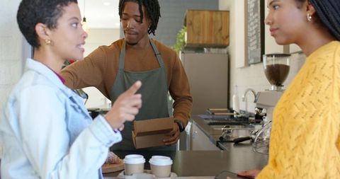 Barista packing takeout while friends chatting at modern cafe counter with coffee cups