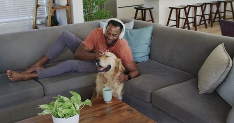 African american man relaxing with golden retriever on gray sofa wearing headphones