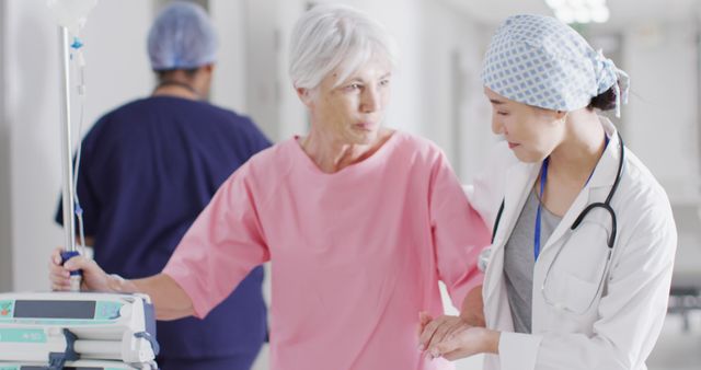 Senior woman in hospital gown holding IV drip, interacting with a caring female doctor in a white coat and stethoscope. This can be used for medical articles, healthcare websites, elderly care brochures and promoting positive patient-doctor relationships.