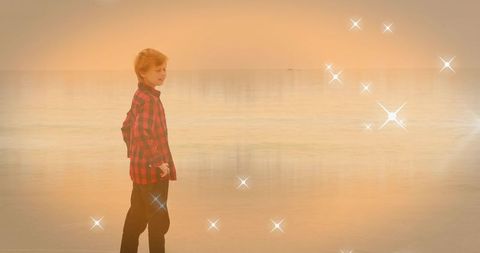 Standing child wearing red plaid shirt at golden sunset shore with sparkling light and calm sea