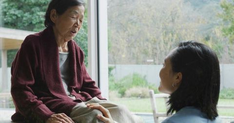 Senior woman receiving gentle caregiving and companionship from adult daughter at window