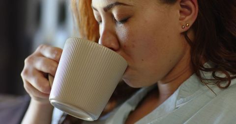 Woman sipping from ribbed ceramic mug closeup, holding warm drink, relaxing morning