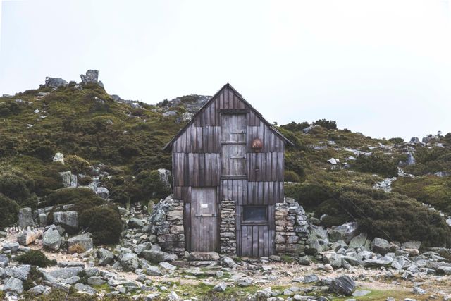 Wooden cabin standing alone in a rocky, mountainous area, surrounded by natural wilderness. Great for themes related to solitude, remote living, nature exploration, or scenic landscapes. Suitable for travel blogs, wilderness adventure marketing, and rustic getaway promotions.