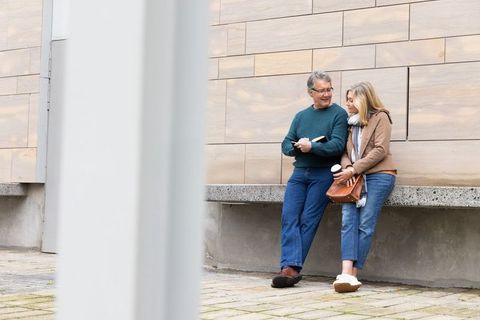 Senior couple chatting on urban ledge holding coffee cup and notebook, casual lifestyle