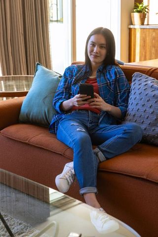Asian Woman Relaxing on Sofa with Smartphone in Chic Living Room