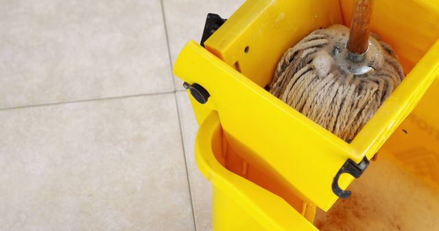 Close up of mop in yellow mop basket with copy space on tiled background. Cleaning, mopping and washing concept.