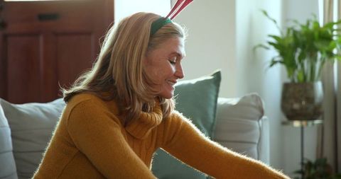 Smiling mature woman wearing green headband with red antlers relaxing on couch