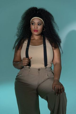 Poised african-american woman sitting holding suspenders wearing beige tank and trousers