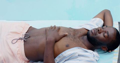 African american man relaxing on poolside towel, enjoying sun and resort leisure
