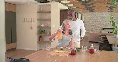 African American man pouring orange juice for smiling woman in rustic loft kitchen
