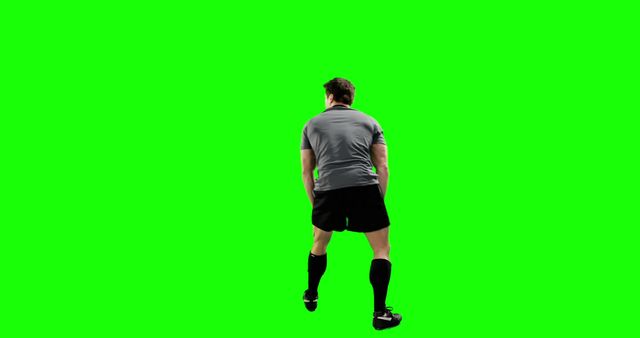 This image shows a rear view of a soccer player standing against a green screen background. The male athlete is dressed in black shorts, a gray shirt, long black socks, and soccer shoes. This image can be used for sports promotional materials, training guides, digital editing purposes, or advertisements related to sports and fitness.