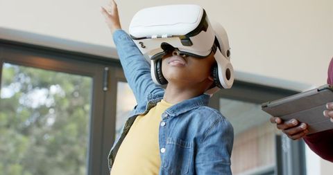 African American Boy Wearing VR Headset Reaching Up While Adult Using Tablet