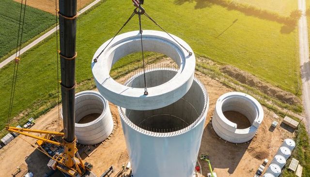 Lattice boom crane lifting precast concrete ring onto wind turbine tower