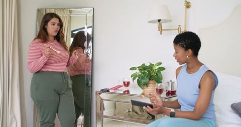 African american women chatting and getting ready in bright bedroom with full-length mirror