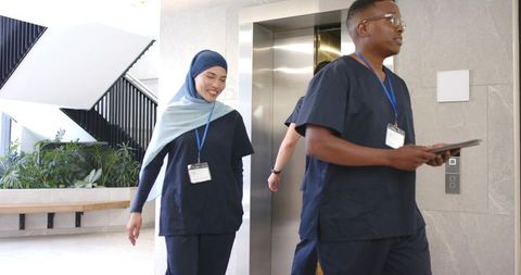 Diverse clinical team walking from elevator in navy scrubs holding tablet, hospital lobby