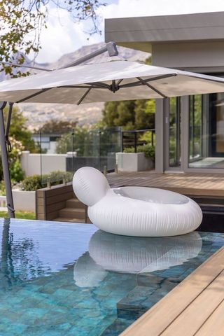 White donut pool float floating at edge of modern backyard pool under umbrella for relaxation