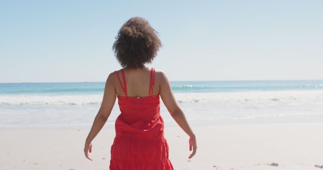 Biracial woman wearing red dress and enjoying sun at beach. Vacation, summer and lifestyle, unaltered.