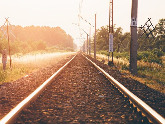 Railroad tracks extending into the distance during sunset in a rural setting, surrounded by fields and trees. This tranquil, scenic view captures the essence of travel and adventure, making it ideal for projects related to journeys, calm evenings, transportation themes, or countryside landscapes.