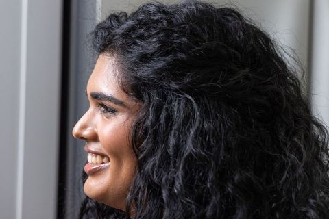 Smiling indian woman showing curly hair texture profile portrait by window light
