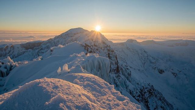 Sunrise bathing snow-covered alpine ridge and icicle-studded summit over glacier