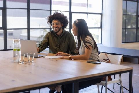 Smiling Coworkers Collaborating on Laptop in Modern Office Workspace