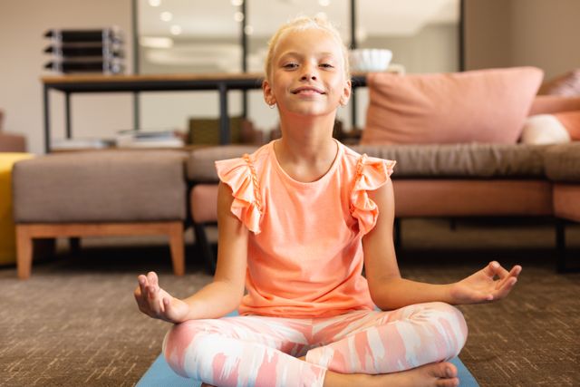 Portrait of smiling caucasian elementary schoolgirl meditating while doing yoga in school. unaltered, childhood, education, yoga, exercising, activity and school concept.