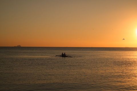 Two Rowers Gliding Across Calm Ocean at Golden Hour Silhouettes and Tranquil Horizon View