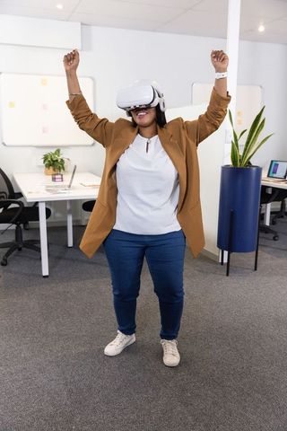 African American woman celebrating while wearing virtual reality headset in modern office