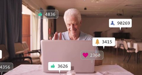 Senior man waving at laptop surrounded by social media notifications and alerts