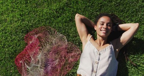 Woman lying on green grass smiling with red mesh tote bag, casual summer relaxation