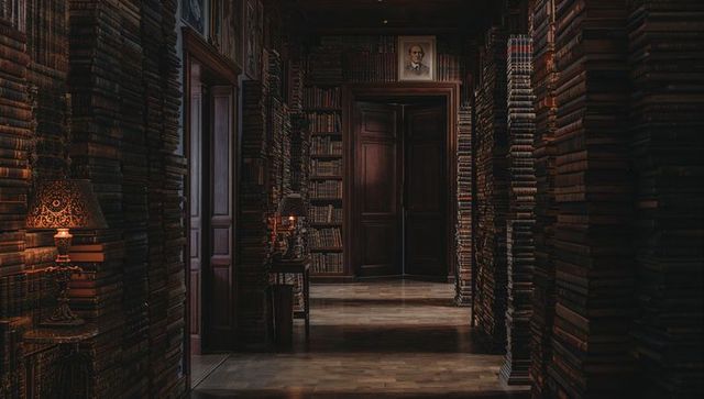 Dimly lit antique library corridor framing central double doors and stacked leather books