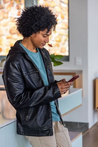 African american man checking smartphone while leaning on modern kitchen countertop