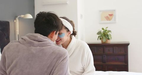Mixed-race couple sharing intimate morning skincare ritual on bed, smiling and relaxing