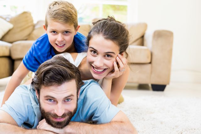 This image of a cheerful family lying on a rug in a cozy living room is perfect for promoting family-oriented products and services, depicting happy moments, or illustrating concepts of home, love, and togetherness. Ideal for use in advertisements, websites, blogs, and social media posts aimed at family bonding and lifestyle themes.