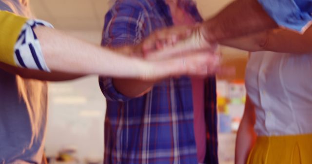 Several individuals in an office place are combining their hands in a gesture of teamwork and collaboration. This scene conveys the spirit of unity and collective effort. Ideal for use in workplace training materials, corporate presentations, team-building outreach, and motivational content highlighting the importance of teamwork.