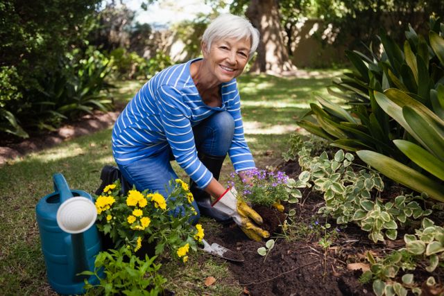 Portrait of smiling senior woman kneeling while planting flowers at backyard