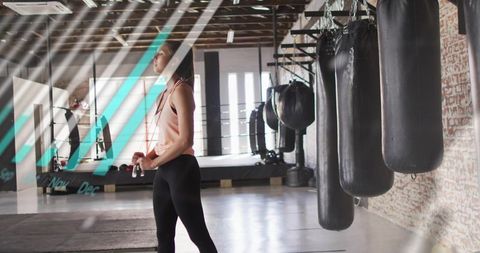 Woman standing holding jump rope gazing toward light by punching bags