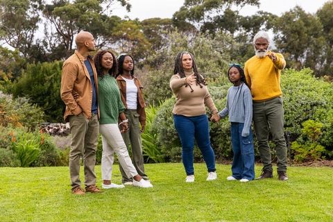Multigenerational african american family standing on green lawn holding hands and pointing