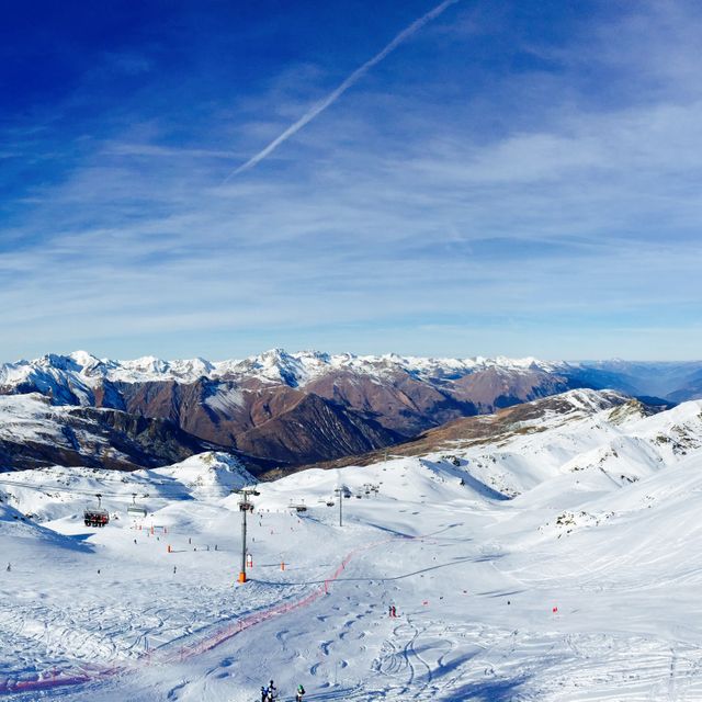 Panoramic view of a snowy mountain ski resort with skiers on slopes under a clear blue sky. Suitable for travel brochures, winter sports advertisements, and tourism promotion for alpine destinations.