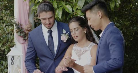 Bride signing wedding document with groom and witness outdoors