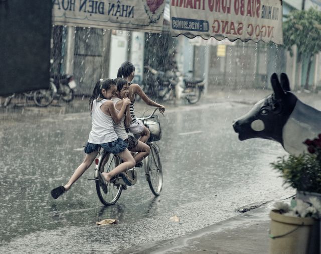 Children riding a bicycle through a rainy street, enjoying a spontaneous adventure. Suitable for content about childhood, outdoor activities, friendship, and summer fun.