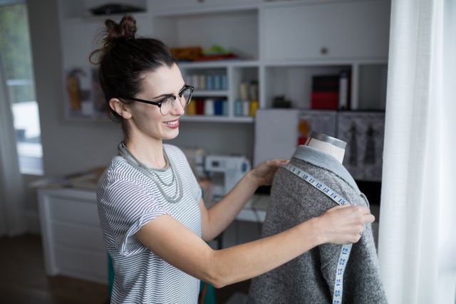 Fashion designer measuring fabric on a mannequin in a home studio. Ideal for content related to fashion design, tailoring, creative workspaces, small businesses, and handmade crafts. Can be used in articles, blogs, or advertisements focusing on the fashion industry, home-based businesses, or creative professions.