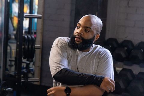 African american man stretching arm in industrial gym with dumbbells and mirror
