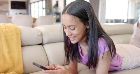 Teenage Girl Relaxing on Couch Using Smartphone Smiling