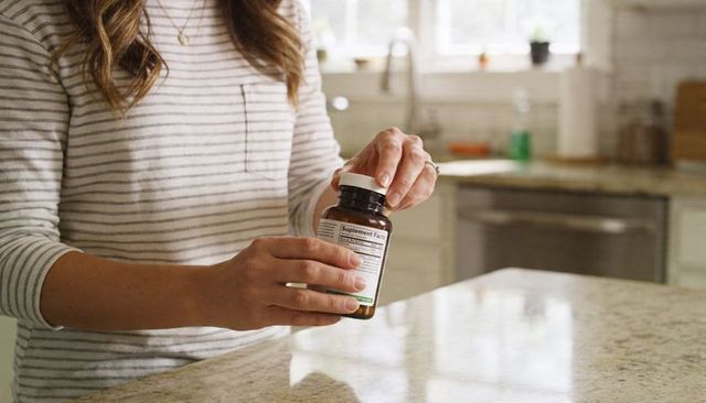 Woman reading supplement label at kitchen countertop holding amber bottle lifestyle