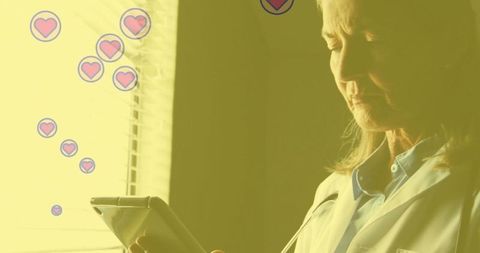 Doctor Engaged with Tablet Surrounded by Heart Icons in Gentle Lighting