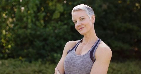 Confident mature woman standing with arms crossed in garden wearing gray activewear