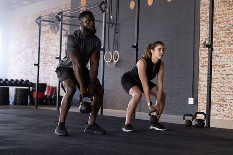 Diverse training partners lifting kettlebells on rubber gym floor in industrial crossfit space