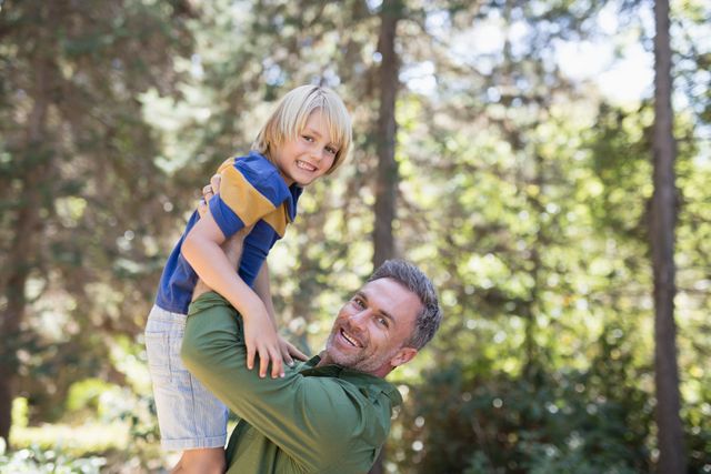 Father lifting son in forest, both smiling and enjoying outdoor time. Ideal for family, parenting, and outdoor adventure themes. Perfect for promoting family activities, nature outings, and joyful moments.