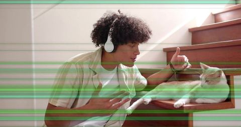 Adult male wearing headphones petting cat on wooden stairs bathed in natural light